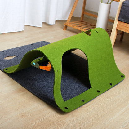 A green tunnel toy made of felt, with a cat sitting beside it and a toy mouse attached to one end.