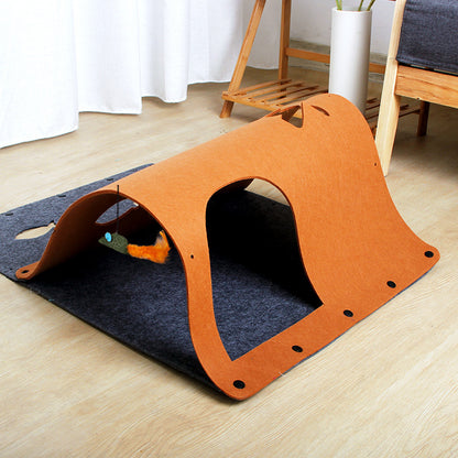 A brown tunnel toy made of felt, with a cat sitting beside it and a toy mouse attached to one end.