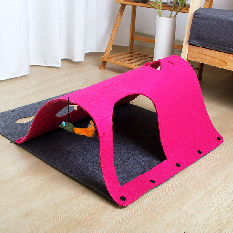 A pink tunnel toy made of felt, with a cat sitting beside it and a toy mouse attached to one end.