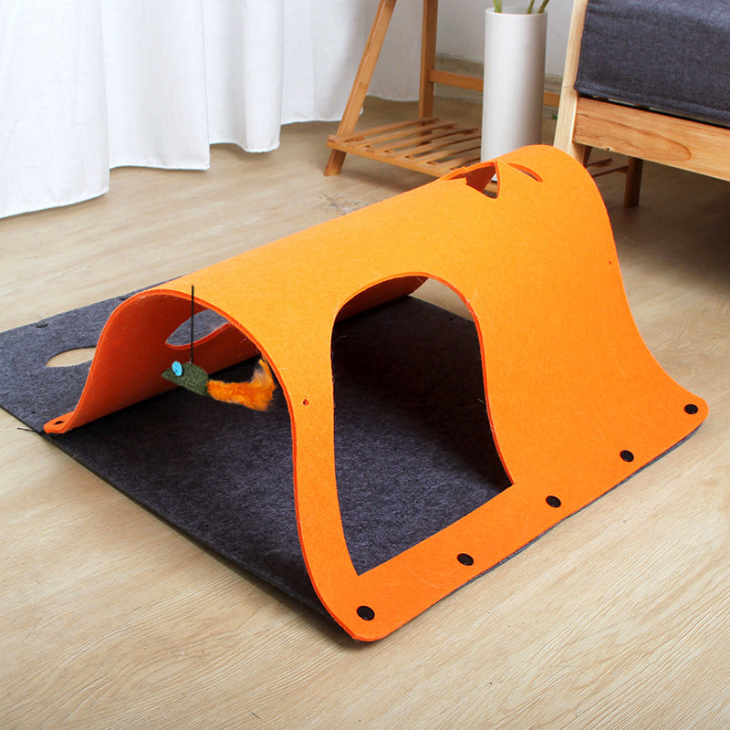 An orange tunnel toy made of felt, with a cat sitting beside it and a toy mouse attached to one end.